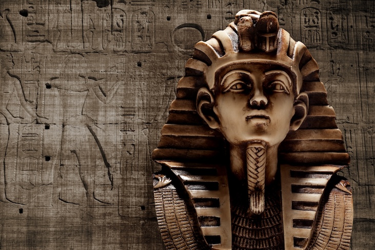 Image of King Tutankhamun's golden mask against a grey stone wall with Egyptian hieroglyphs.
